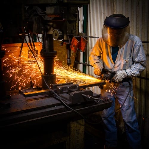 man with welding helmet and other protective gear on welding with sparks flying